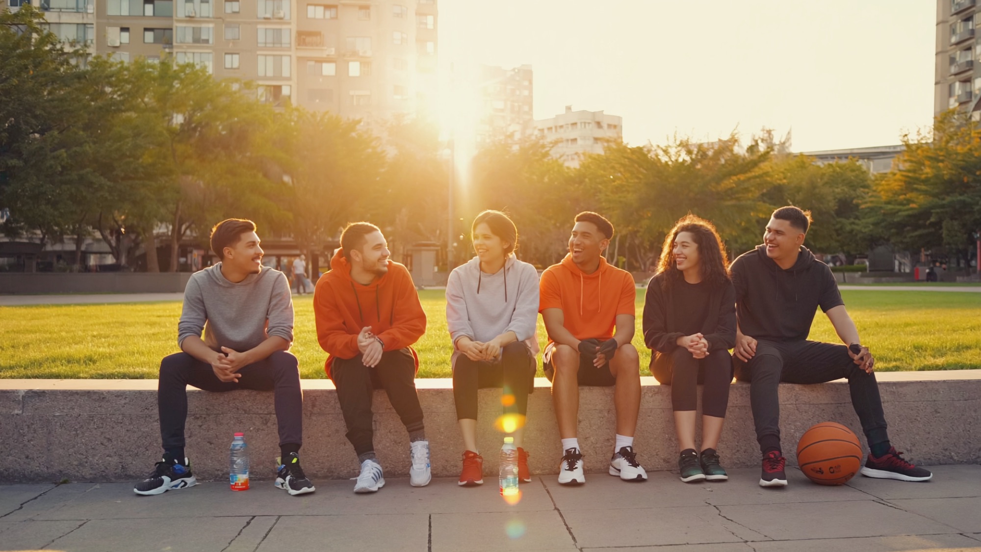 A crew of friends laughing together in the park after a workout at golden hour